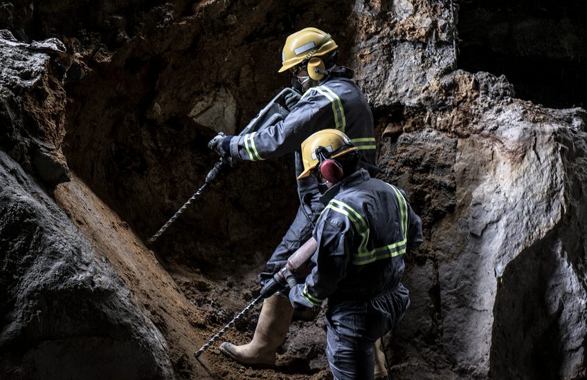 Two workers with helmet and protective suit using drill-machines in an underground enviroment